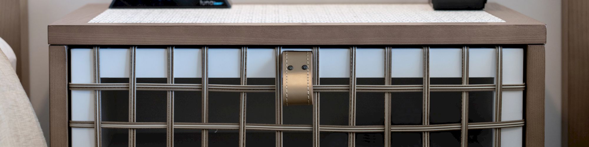 The image shows a nightstand with a digital clock and an electronic device on top, positioned between two beds.