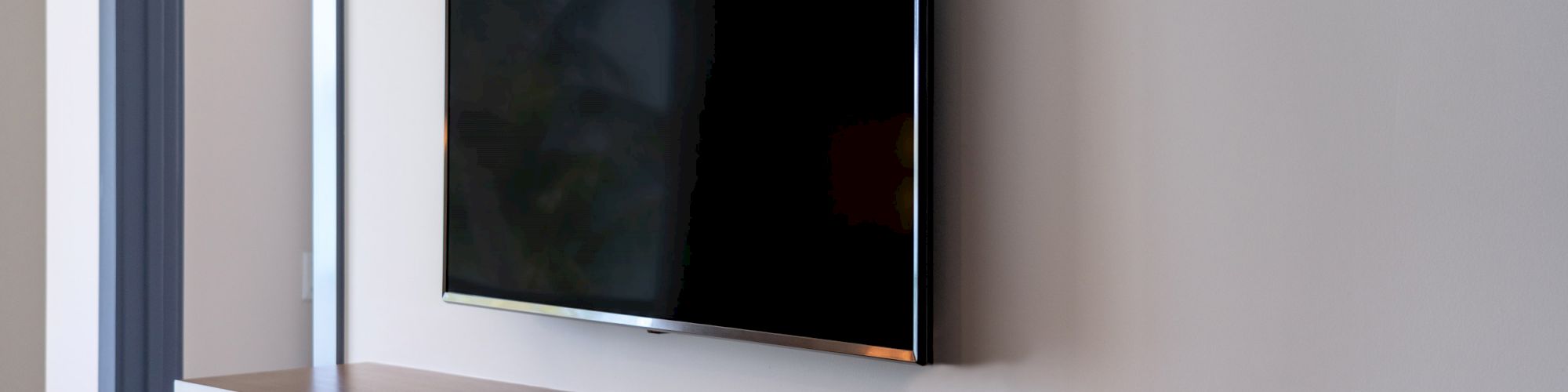 A flat-screen television is mounted on the wall above a floating shelf, with a partially visible sliding door next to it.