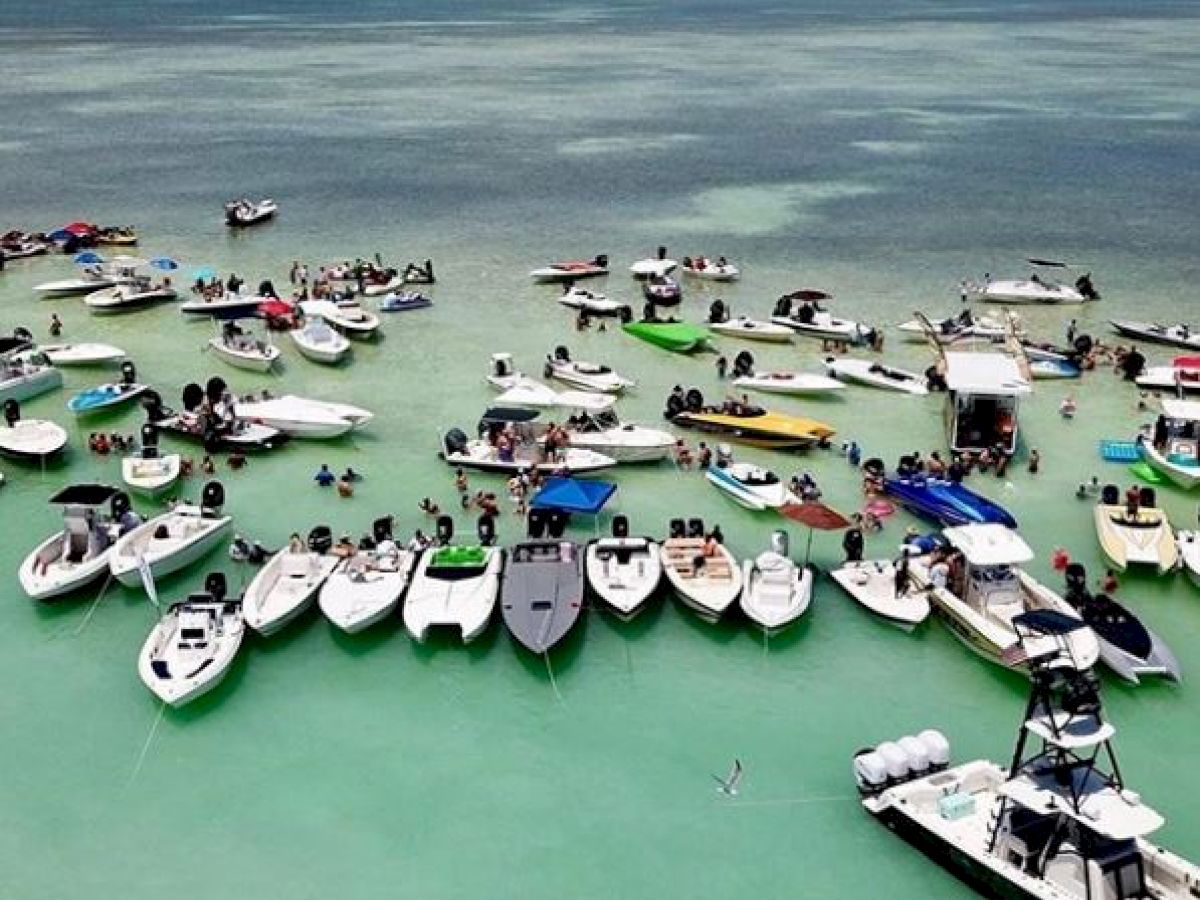 A gathering of numerous boats anchored in a shallow, clear turquoise water area, with people socializing and enjoying the day.