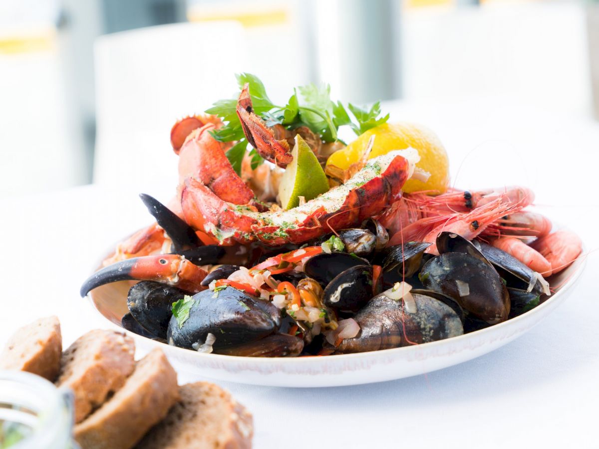 A seafood platter with various shellfish, including shrimp, crab, and mussels, garnished with herbs and lemon, served on a white plate.