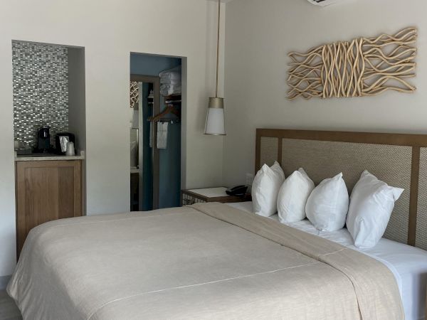 A hotel bedroom with a king bed, white pillows, ceiling fan, wall art, and a wall-mounted air conditioner.