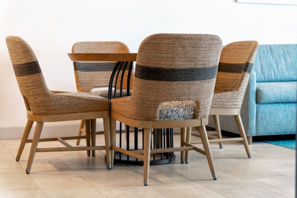 The image shows a set of four beige upholstered chairs around a small round table on a tiled floor, with a blue sofa in the background.