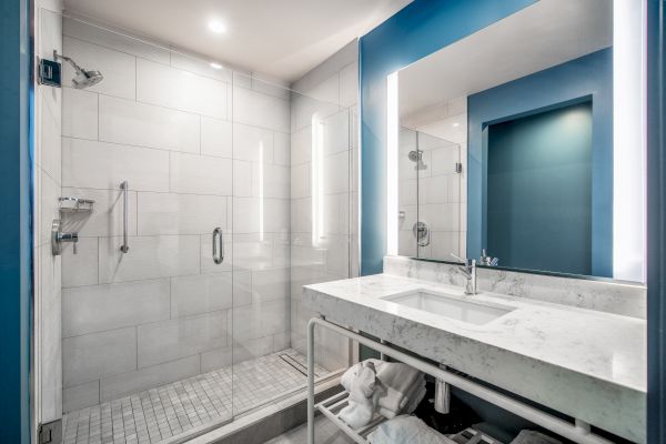 A modern bathroom with a glass shower, white tiles, a marble countertop sink, a large mirror, and neatly stored towels under the sink.