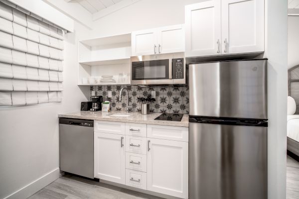 A modern kitchen with white cabinets, a stainless steel refrigerator, microwave, dishwasher, coffee machine, toaster, and decorative backsplash ending the sentence.