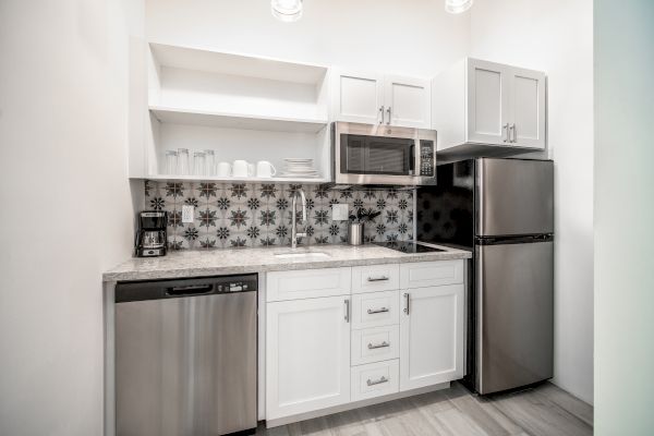 A modern kitchen with stainless steel appliances, including a dishwasher, microwave, and refrigerator, white cabinets, and a patterned backsplash.