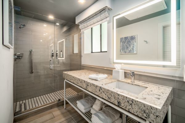 A modern bathroom with a glass shower, illuminated mirror, and granite countertop. Towels and toiletries are neatly arranged below the sink.