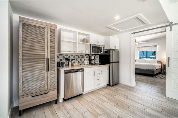 Modern kitchen with light wood floors, stainless steel appliances, and a view into a spacious bedroom through a sliding door.