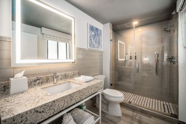 A modern bathroom with a granite-topped vanity, illuminated mirror, glass shower, and neatly organized towels and toiletries.