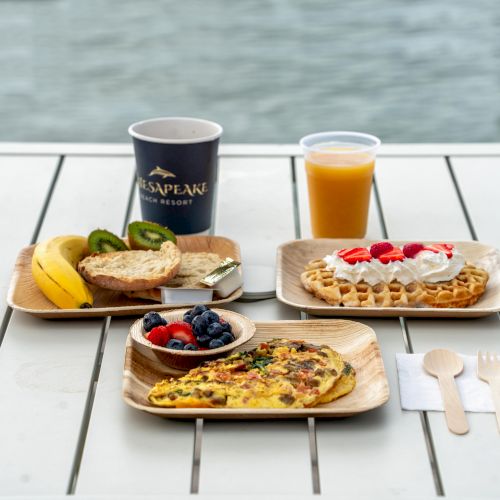 A breakfast spread with an omelette, toast, fruit, waffle with cream and strawberries, coffee, and orange juice on a table.