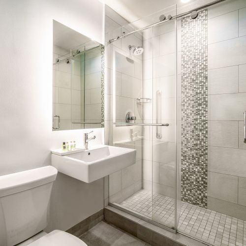 A modern bathroom with a toilet, sink, and glass-enclosed shower featuring tiled walls and a mosaic strip.