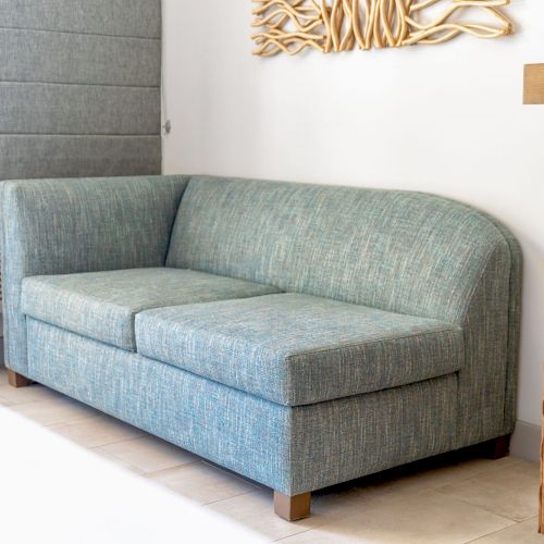 The image shows a light blue sofa in a modern room with a wall decoration and a window air conditioner.