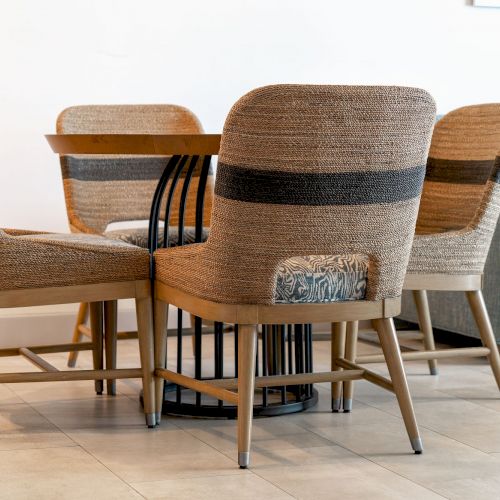 A set of four woven chairs arranged around a round wooden table on a tiled floor, with a blue sofa in the background.