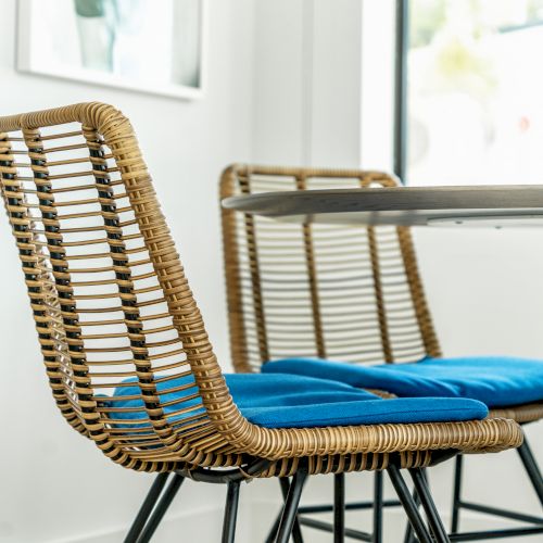 The image shows wicker chairs with blue cushions around a white table in a bright, modern room setting.