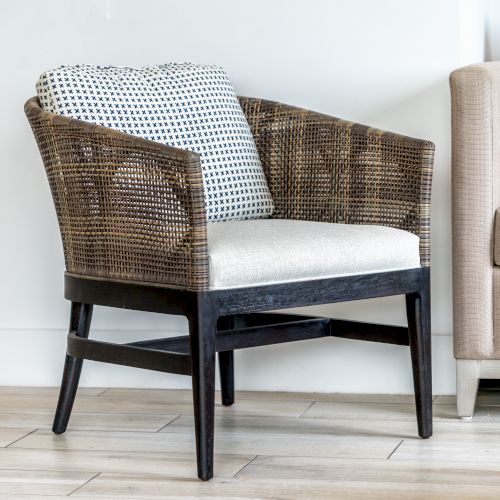 The image shows a wicker chair with a patterned cushion next to a beige sofa on a wooden floor, set against a white wall.