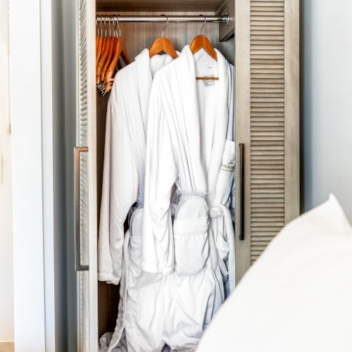 The image shows an open wardrobe with several white bathrobes on hangers inside a well-lit room.