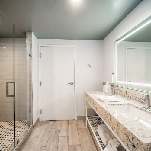 A modern bathroom with a glass shower, a double vanity with a marble countertop, and an illuminated mirror.