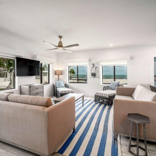 Bright living room with large windows, beige sofas, blue-striped rug, and coastal view. Casual, relaxed decor with a modern touch.