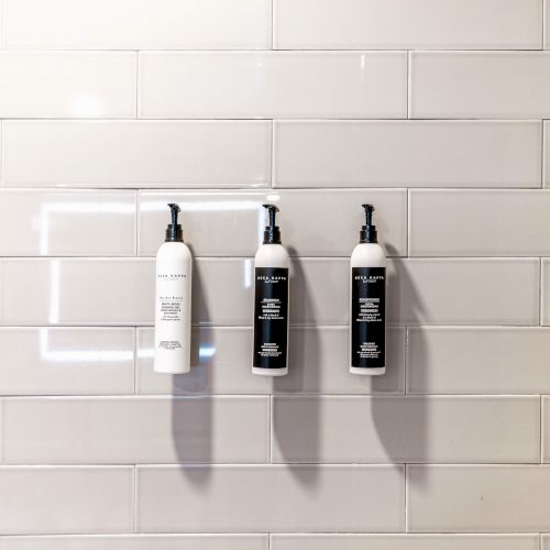 The image shows three pump bottles mounted on a tiled wall, likely containing personal care products like shampoo or body wash.