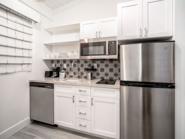 A modern kitchen with white cabinets, a stainless steel refrigerator, microwave, dishwasher, coffee machine, toaster, and decorative backsplash ending the sentence.