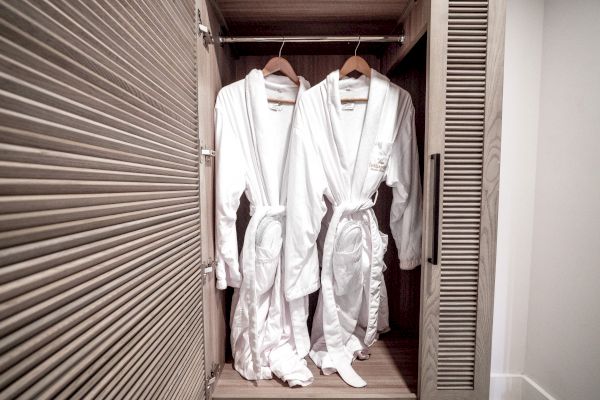 Two white bathrobes hanging inside a wooden closet on hangers, neatly arranged with the closet door partially open.