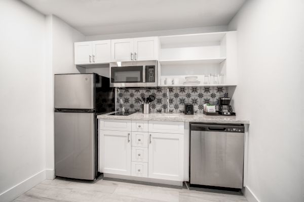 The image shows a modern kitchen featuring a refrigerator, microwave, dishwasher, and white cabinets with a patterned backsplash.