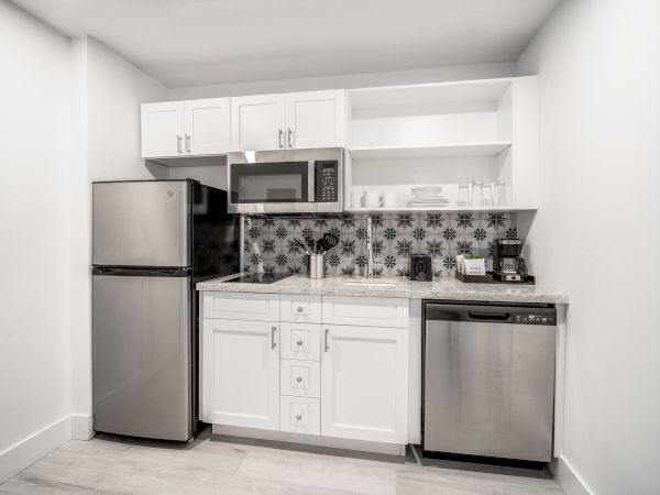 The image shows a modern kitchen featuring a refrigerator, microwave, dishwasher, and white cabinets with a patterned backsplash.