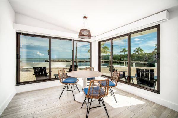 A bright, modern dining area with large windows offering a view of a tropical outdoor scene, featuring a round table and four chairs.