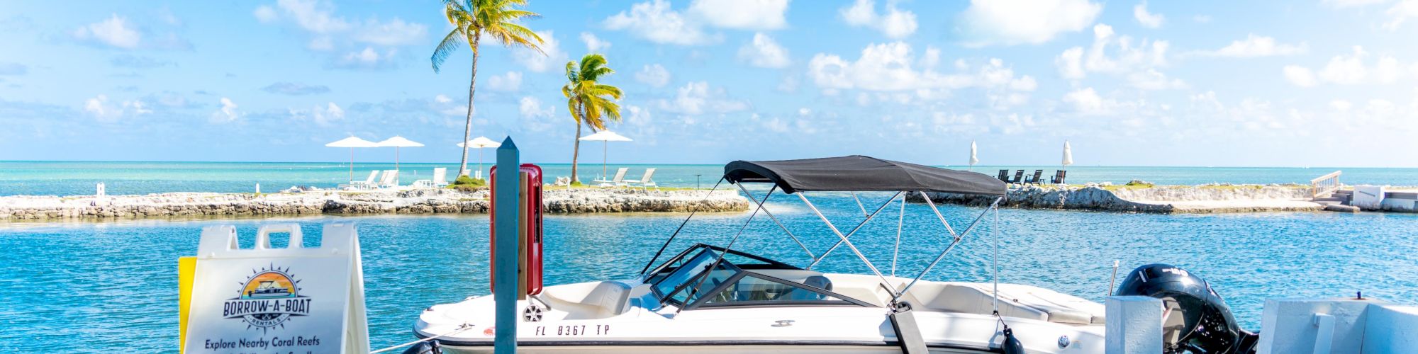 A boat is docked at a marina under a bright blue sky, with a sign advertising boat rentals in the foreground.