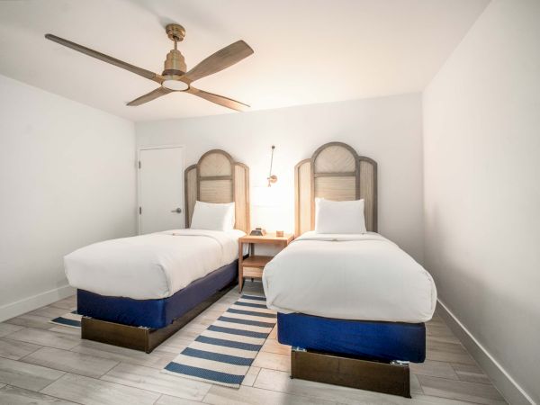 A bright bedroom with a ceiling fan and two twin beds with arched wooden headboards and pillows.
