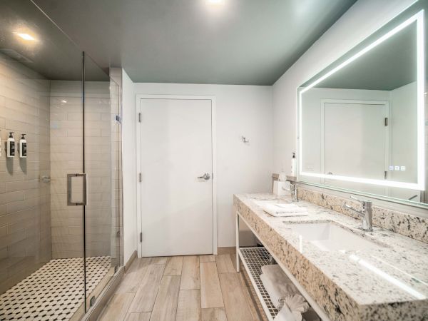 Modern bathroom with glass shower, tiled walls, granite vanity and a backlit mirror over a sink.