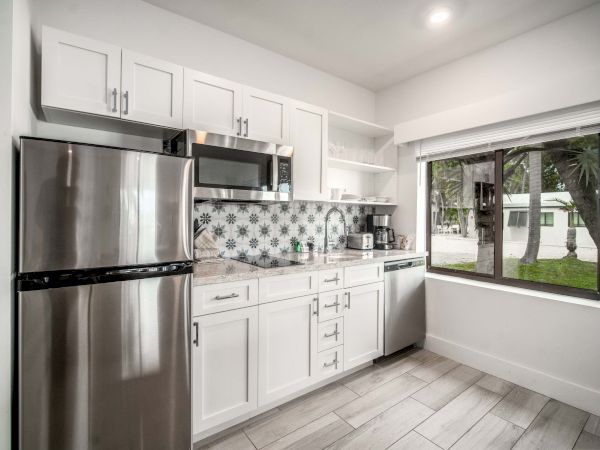 Bright kitchen with a stainless fridge, white cabinets, microwave, patterned tile backsplash, and a large window to the yard.