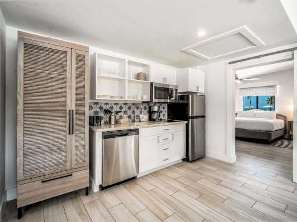 A modern kitchen with white cabinets, granite counters, stainless appliances, and a doorway showing a bright bedroom with ocean views.