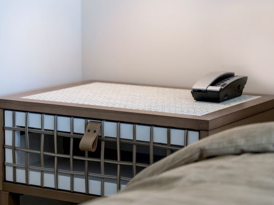 A neatly made bed with a metal frame and a black device placed on the mattress, in a quiet room.