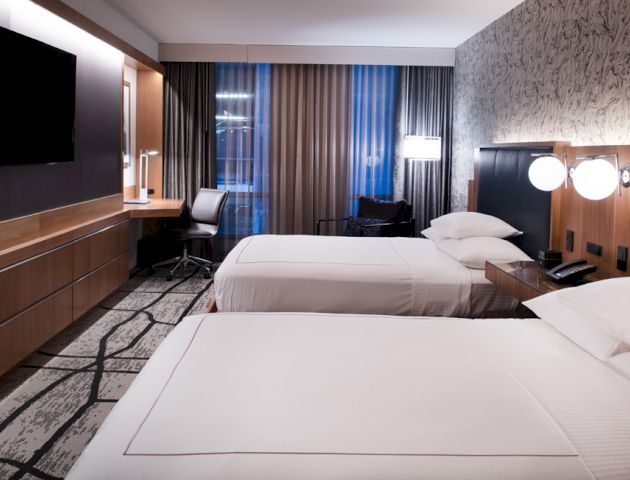 A modern hotel room featuring two neatly made beds, a wall-mounted TV, a desk with a chair, and stylish decor.
