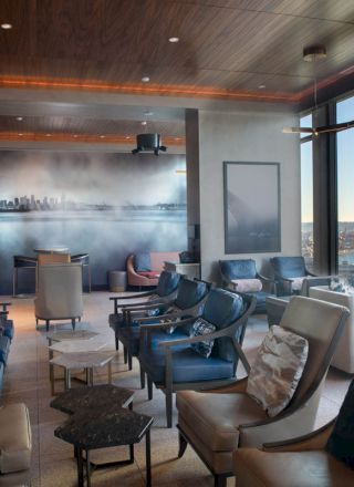 A modern lounge with large windows offering a scenic view of the water and a Ferris wheel, furnished with comfortable chairs and small tables.