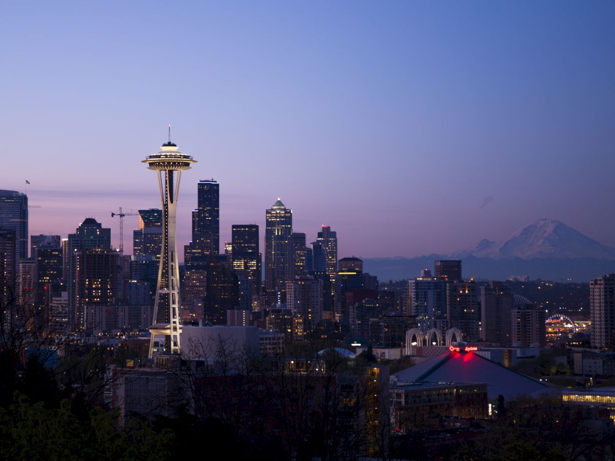 The image shows the Seattle skyline at twilight, featuring the Space Needle, numerous skyscrapers, and Mount Rainier in the background.